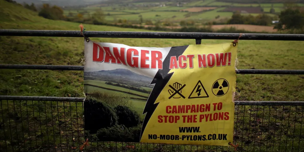 A protest banner against a new power line is displayed on a farm gate in the UK.