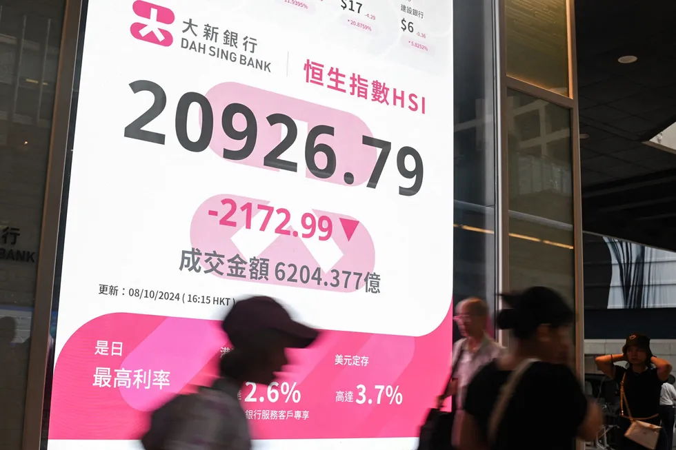 Pedestrians walk past a sign showing the numbers of the Hang Seng Index in Hong Kong on 8 October 2024. Hong Kong stocks plunged more than 9%, their biggest fall in 16 years, after China left investors disappointed by a lack of new stimulus and few details about measures announced last month.