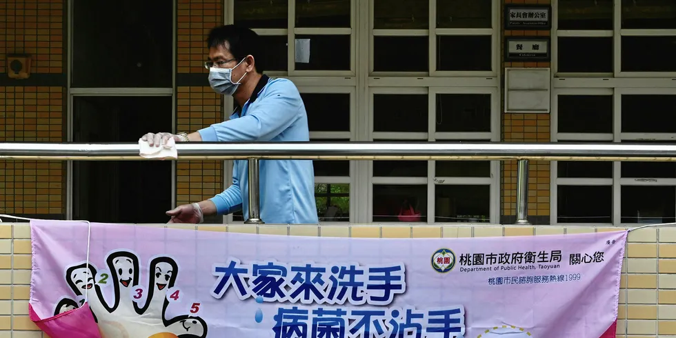 A man wears a face mask while cleaning a handrail behind a sign telling students how to wash their hands to prevent the COVID-19 corona virus at a middle school in Taoyuan, northern Taiwan