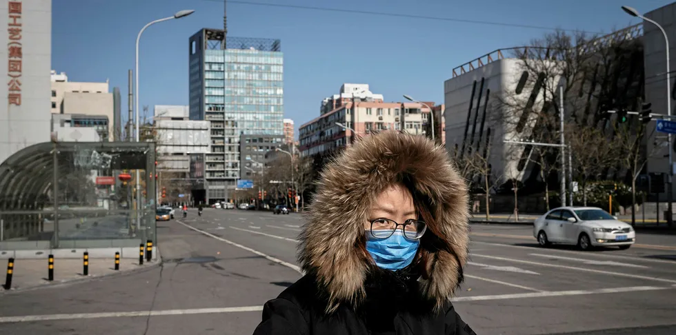 The impact of the coronavirus: a woman wearing a protective facemask cycles along a nearly empty street in Beijing