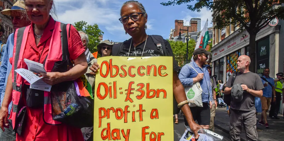 A protester holds a placard stating that oil companies have been making a profit of £3 billion per day for 50 years.