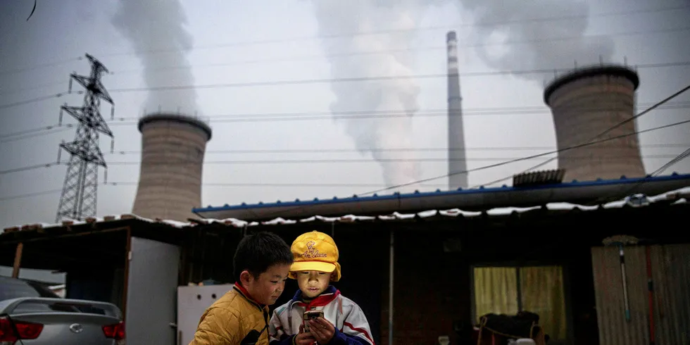 BEIJING, CHINA - NOVEMBER 27: Chinese boys look at their smartphone in front of their house next to a coal fired power plant on November 27, 2015 on the outskirts of Beijing, China.