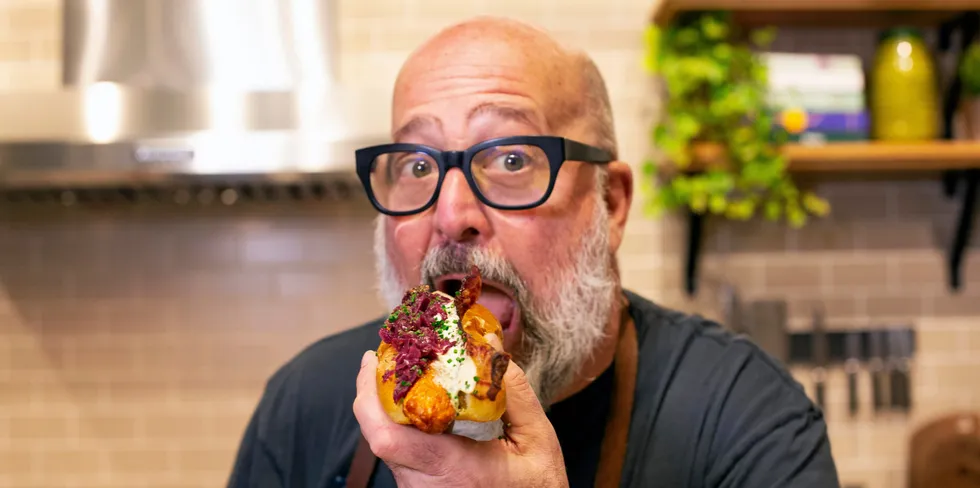 Chef Andrew Zimmern tucks into a Kvaroy salmon dog with cabbage, bacon and tartare sauce.