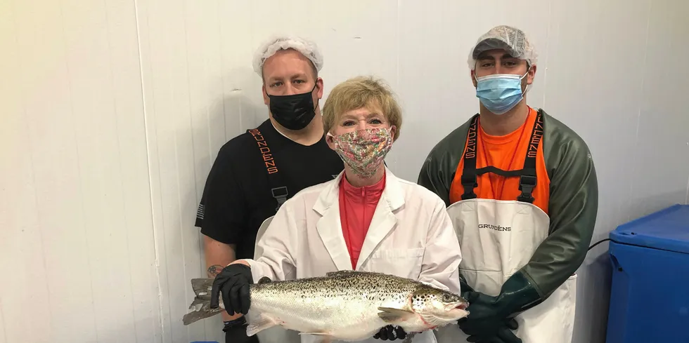 . AquaBounty Processing Associates Skyler Miller (left) and Jacob Clawson (right), with CEO Sylvia Wulf (center) holding the first commercially harvested genetically modified farmed salmon in the US.