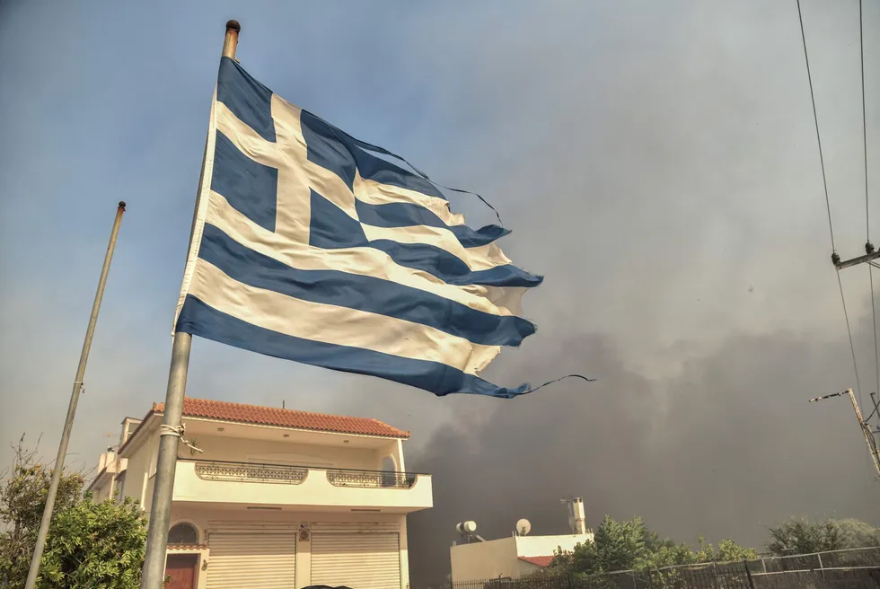 A Greek flag flutters in the wind during a wildfire southeast of Athens in 2023.
