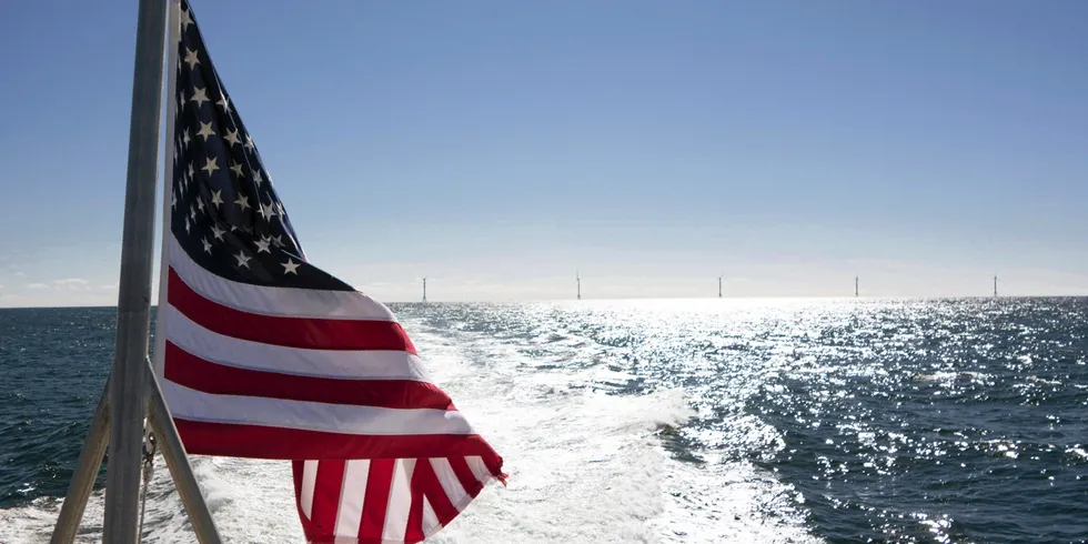 An US flag flies as the five towers of the Block Island Wind Farm stand in the water.