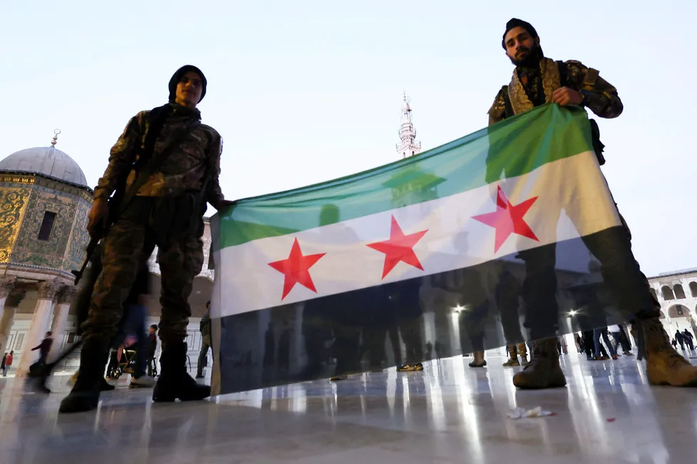 Rebel fighters pose as they hold a Syrian opposition flag inside the Umayyad Mosque after rebels seized the capital and ousted Syria's Bashar al-Assad, in Damascus, Syria.
