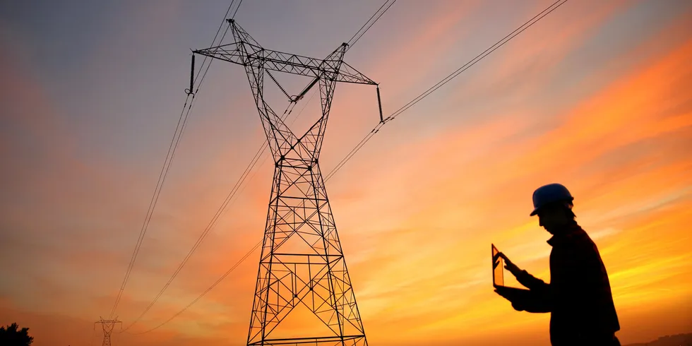 An electrical engineer with a laptop near a high-voltage transmission pylon.