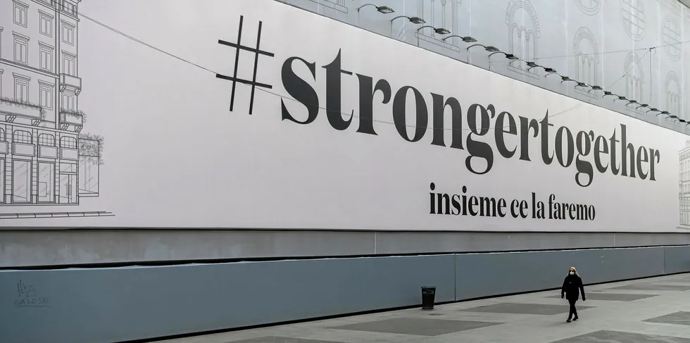 A woman wearing a protective mask walks in a deserted street past a giant billboard reading "#strongertogether, together we'll make it" on March 31, 2020 in Milan, during the country's lockdown aimed at curbing the spread of the COVID-19 infection.