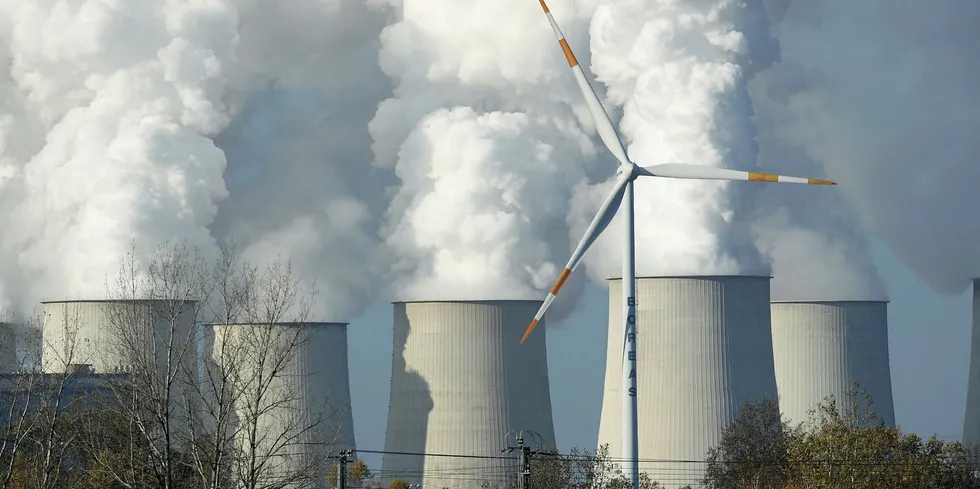 A wind turbine spins as steam rises from the cooling towers of the Jaenschwalde coal-fired power plant in Germany