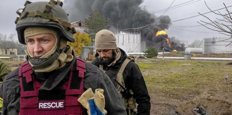 A Ukrainian rescue service member and a soldier inspect the area as black smoke rises after an attack on an oil reserve in Kherson.