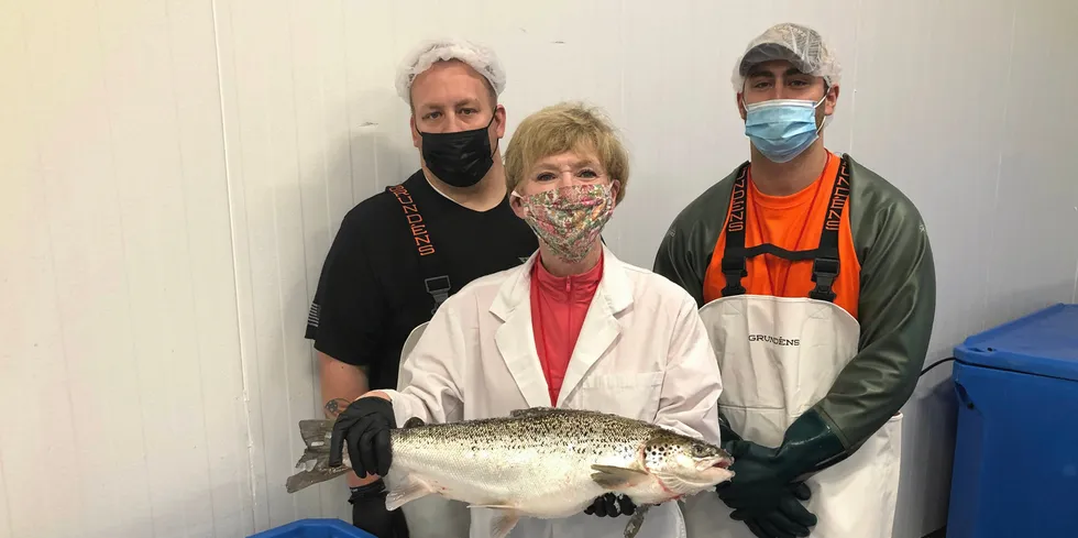 AquaBounty processing associates Skyler Miller (left) and Jacob Clawson (right), with CEO Sylvia Wulf (center) holding the first commercially harvested genetically modified farmed salmon in the US.