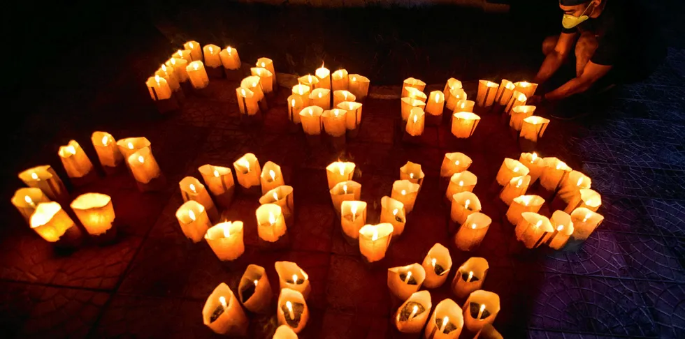A volunteer arranges lit candles in a formation to read 'Fight Covid-19' during the Earth Hour environmental campaign near a catholic church in Borongan City, in the Philippines