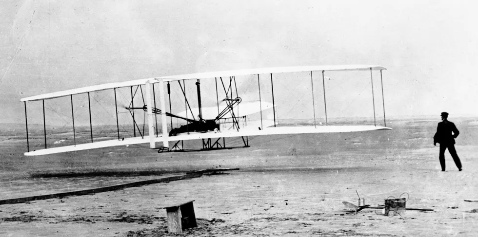 Orville Wright piloting the world's first powered flight at Kitty Hawk, North Carolina, in 1903, as his brother Wilbur looks on.