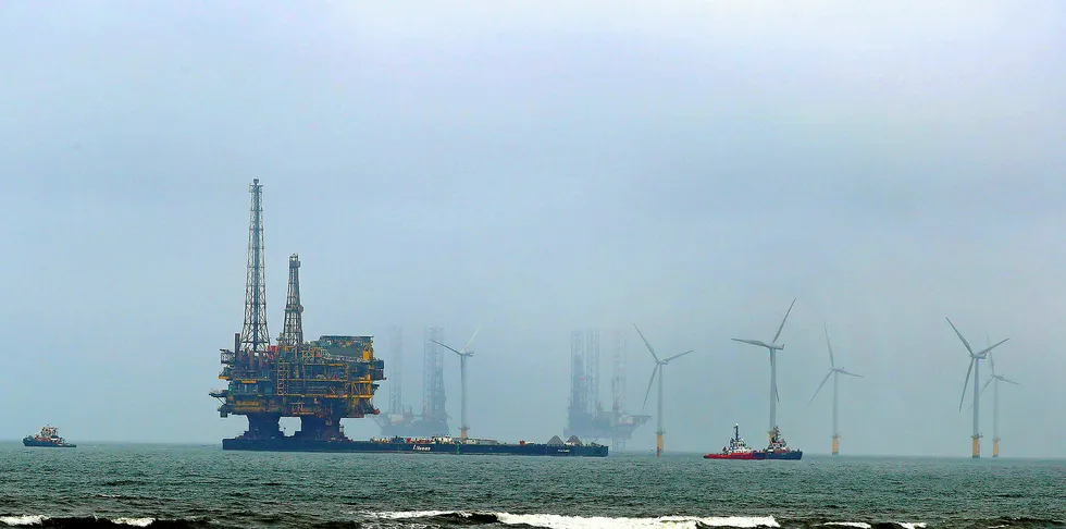A decommissioned Shell offshore oil drilling platform being towed past an offshore wind farm off the UK.
