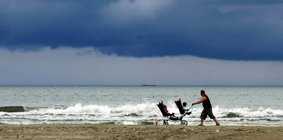 A man pushes a pram with two children on the Black Sea beach after a heavy rain in Navodari, Romania