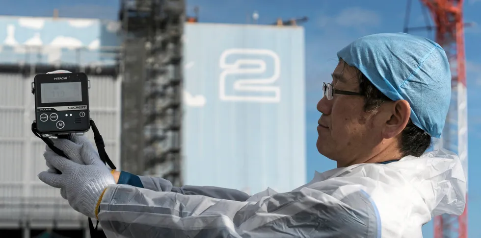 An employee shows a dosemeter as he measures radiation in front of the Unit 2 reactor building at Tokyo Electric Power Co.'s (Tepco) Fukushima Dai-ichi nuclear power plant.
