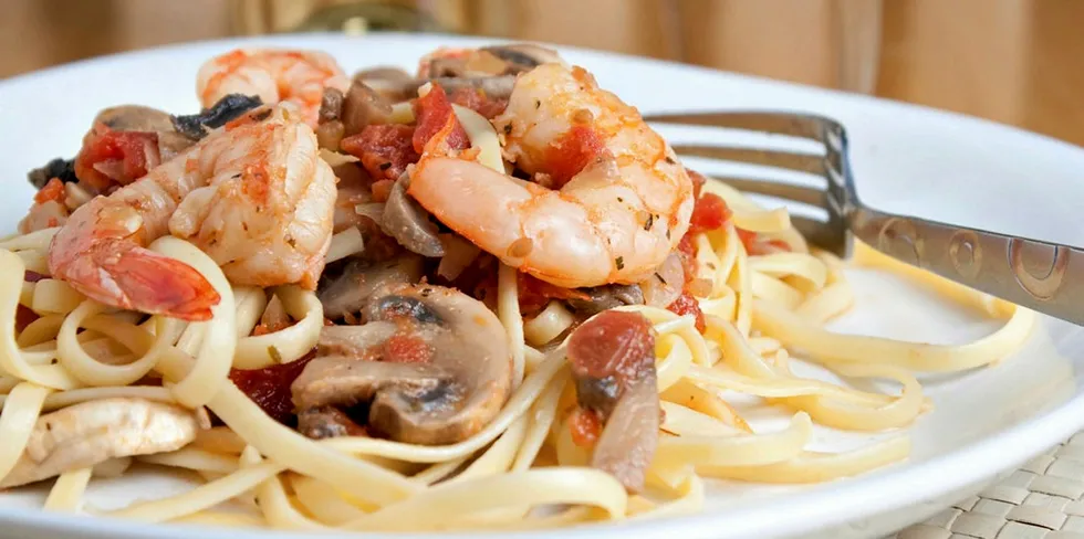 A delicious shrimp scampi pasta dish with mushrooms and diced tomatoes along with a glass of pinot grigio white wine.