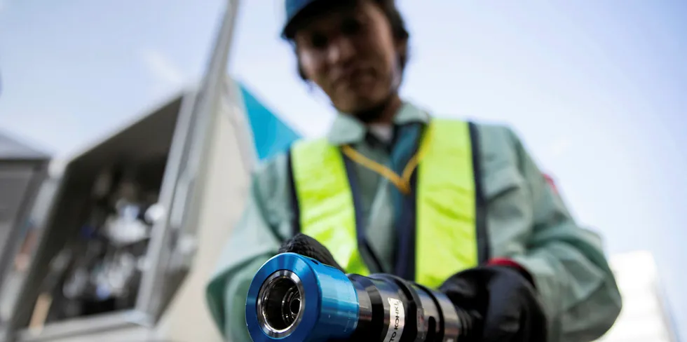 A worker holds a hydrogen fuel- pump nozzle at a low-carbon hydrogen supply-chain demonstration project in Yokohama, Japan