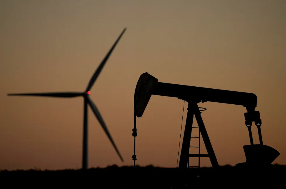 A pumpjack operates in the foreground while a wind turbine at the Buckeye Wind Energy wind farm rises in the distance.