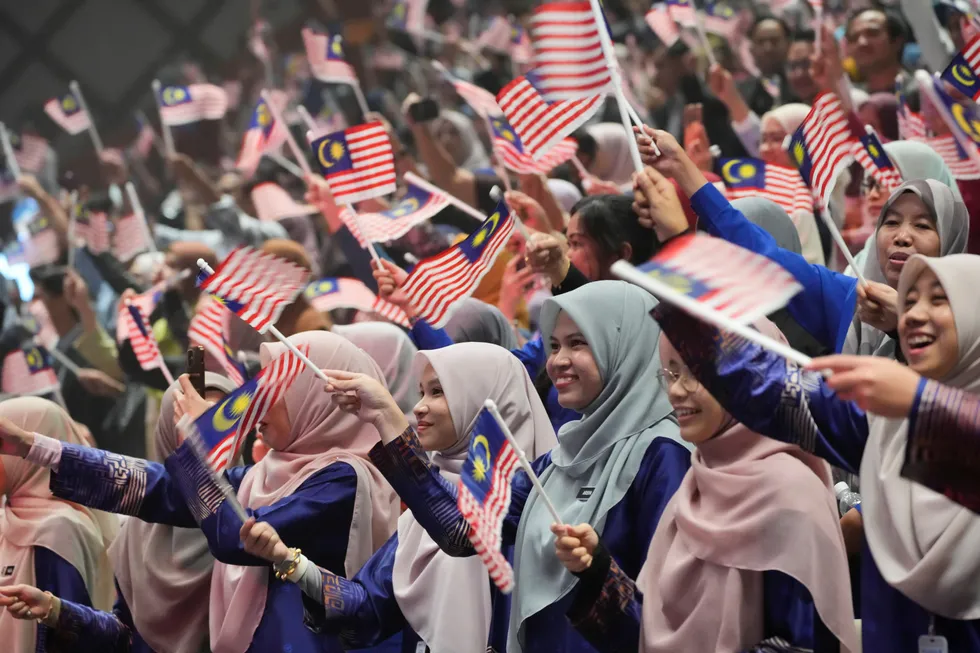 A group waves national flag during a gathering for National Day at a convention centre in Putrajaya, Malaysia.