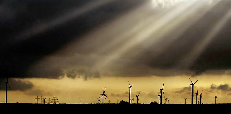 Sunbeams shine through dark clouds on a field of turbines in Germany.
