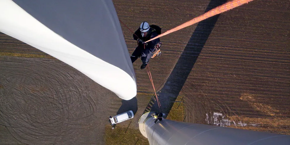 A technician assesses the rotor blade and tower of a wind turbine.