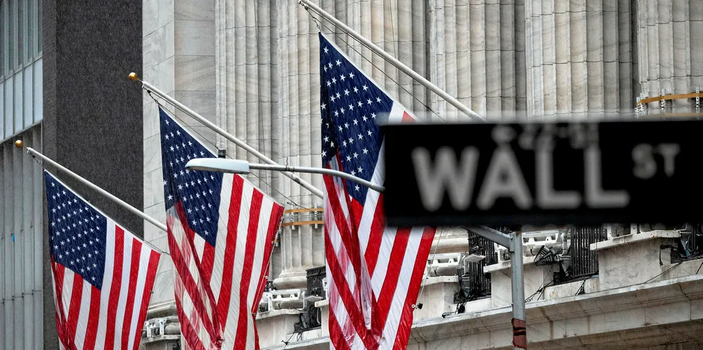 The "Wall St" street sign is seen near US flags in front of the New York Stock Exchange (NYSE) on a rainy day on Wall Street in New York City.
