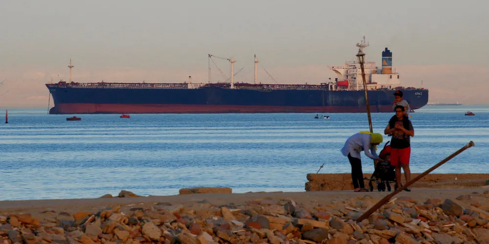 People walk on the beach as a tanker crosses the Gulf of Suez towards the Red Sea before entering the Suez Canal.
