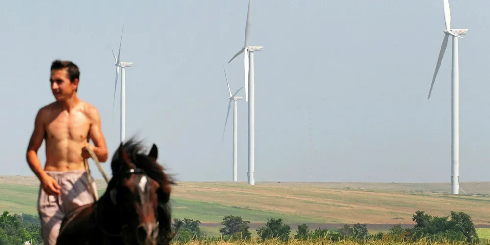 A man rides a horse next to wind farm in Cogealac, Romania