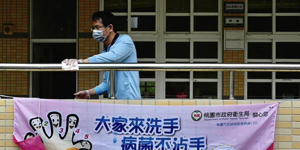 A man wears a face mask while cleaning a handrail behind a sign telling students how to wash their hands to prevent the COVID-19 corona virus at a middle school in Taoyuan, northern Taiwan