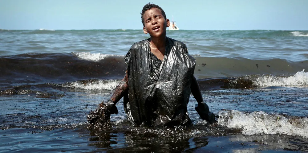 A boy walks out of the sea while removing oil spilled on Itapuama beach in Pernambuco state, Brazil, on 21 October 21 2019. The source of the patches remain a mystery despite President Jair Bolsonaro's assertions they came from outside the country and were possibly the work of criminals