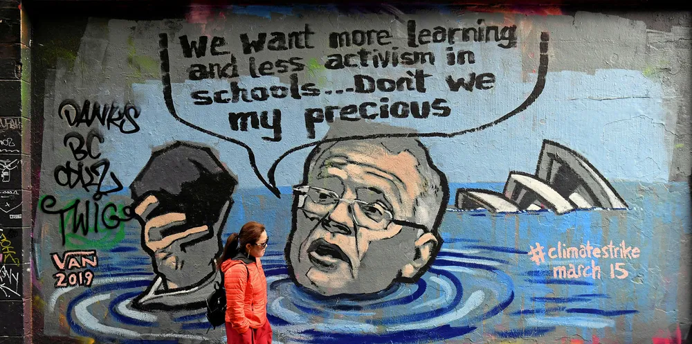 A tourist walks past a mural showing Australian Prime Minister Scott Morrison holding a lump of coal as it advertises a rally by students around the world to protest against climate change, in Melbourne on March 12, 2019.