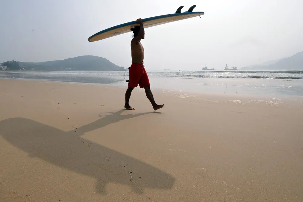 Marine activities: a surfer carries his board toward the waters of the South China Sea on the southeast coastline of China's southernmost island province of Hainan