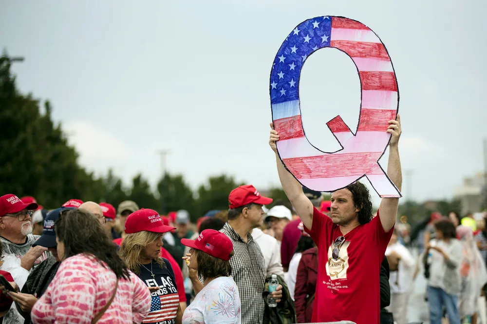 En demonstrant holder en stor Q mens han venter på å komme inn på et valgkampmøte med president Donald Trump i Pennsylvania i begynnelsen av august.
